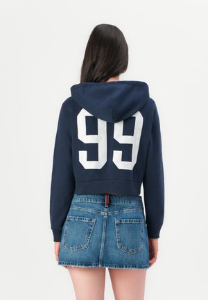 Navy cropped hoodie with white "99" print on the back, paired with a blue denim mini skirt featuring back pockets and frayed hem.