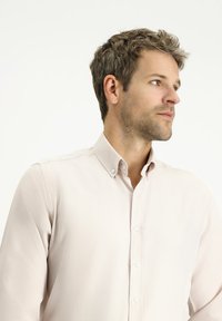 Camicia button-up rosa chiaro con tessuto testurizzato e colletto; presenta bottoni bianchi, stile aderente e maniche lunghe.