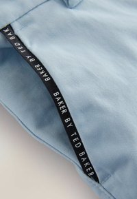 Jasnoniebieska tkanina o gładkiej fakturze. Na krawędzi znajduje się czarna metka z białym napisem „BAKER BY TED BAKER”.