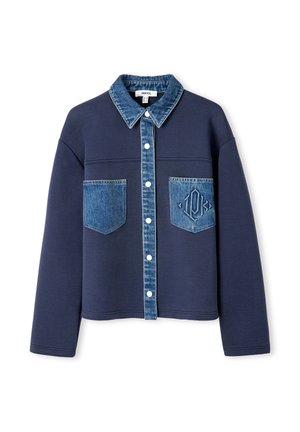 Giacca blu navy con colletto in denim e tasche, con chiusura a bottone, texture di tessuto a contrasto e un logo in rilievo discreto su una tasca.