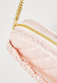 Ružová saténová prešívaná taška so zlatým zipsom a kovovými prvkami. Obsahuje zhromaždený, textúrovaný popruh na nosenie. Kompaktný a guľatý dizajn.