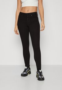 Jeans skinny negros de cintura alta, con cierre de cinco botones y bolsillos frontales. Combinados con zapatillas deportivas negras y amarillas.