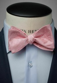 Vaaleanpunainen paisley-kuvioinen silkkinen solmio, jossa on tekstuuripinta, esillä puseron päällä tumman bleiserin alla.