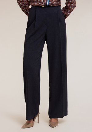 Pantaloni a gamba larga blu scuro con vita alta e pieghe anteriori, realizzati in un tessuto strutturato, abbinati a scarpe con tacco beige.