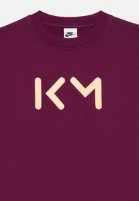 Felpa color bordeaux con colletto rotondo e grande grafica in contrasto "KM" di colore arancione chiaro con dettagli a strisce sul davanti.