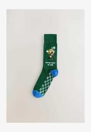 Chaussettes vertes avec un graphisme de personnage de dessin animé, accents bleu au bout et au talon, et le texte "NON NON PAS DE TROU EN UN" en lettres blanches.