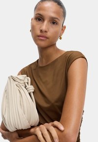 Brązowy dopasowany top z krótkimi rękawami, trzymający kremową plisowaną torebkę z węzłową rączką. Wyraźna gładka tekstura i miękkie detale tkaniny.