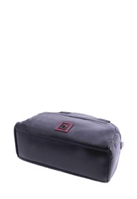 Neceser de piel negra con forma rectangular, textura suave y un parche de marca rojo en la parte frontal. Cierre de cremallera en la parte superior.