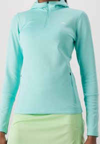 Světle modrá pánská mikina s dlouhým rukávem, na zip, s vysokým límcem, přiléhavým střihem a hladkým materiálem. Obsahuje malé logo na hrudi a kapsy na zip.