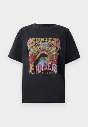 T-shirt en coton noir avec un design graphique coloré comprenant des fleurs, des rayons de soleil, et le texte "SUNSET ROXY CHASER Depuis 1990" soigneusement affiché.