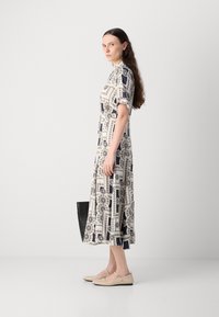 Printed midi dress with short sleeves, featuring a geometric navy and cream pattern. Worn with beige flats and a black tote bag.