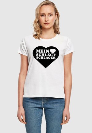 Balta medvilninė marškinėliai trumpomis rankovėmis su juodu širdies grafiku ir baltu tekstu: "MEIN ♥ SCHLÄGT SCHLAGER." Klasikinis kirpimas, laisvalaikio stilius.