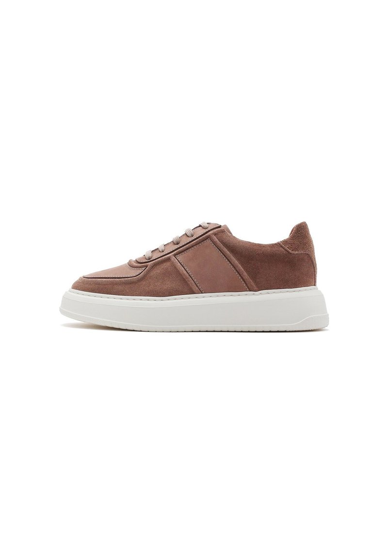 Baskets en daim marron avec semelle en caoutchouc blanche, présentant un accent en cuir lisse et des lacets gris. Bout arrondi et design minimaliste.