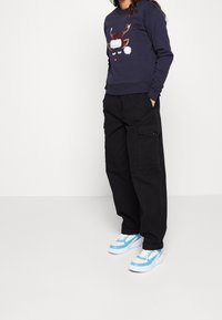 Felpa blu navy con motivo renna, pantaloni cargo neri e sneakers con dettagli blu. Presenta tessuti morbidi e vestibilità casual con tasche.