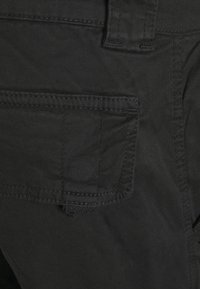 Black cotton fabric with a front pocket, featuring a rectangular shape and visible stitching details. Texture appears smooth and durable.