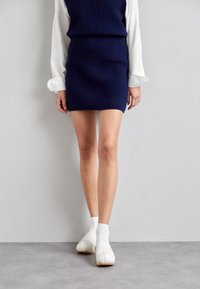 Falda mini de punto azul marino combinada con una blusa blanca de manga larga. Zuecos blancos con suelas de madera y calcetas acanaladas completan el look.