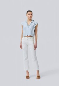 Blauw-witte gestreepte crop top met korte, gerimpelde mouwen, knoopsluiting aan de voorkant, gecombineerd met witte flared jeans en bruine instap sandalen.