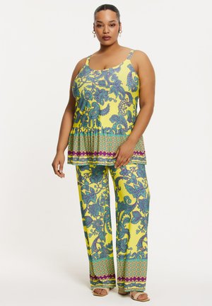 Gele gestippelde tweedelige outfit met een peplumtop met blauwe en paarse bloemenontwerpen en loszittende broek met bijpassende patronen.