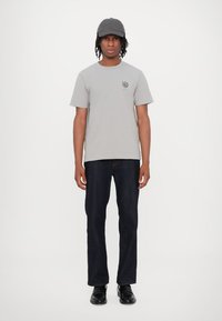 Gray t-shirt with a logo on the chest, paired with dark denim jeans and black shoes. The person is wearing a gray cap.
