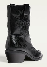 Stivale da cowboy in pelle nera con design ricamati, punta affusolata e tacco di altezza media con texture. Presenta un'apposita linguetta per facilitare l'indossamento.