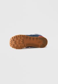 Semelle de sneaker bleu marine avec semelle extérieure en caoutchouc couleur gomme, dotée de profondeurs de sculpture, logo latéral visible et détail rouge au talon.