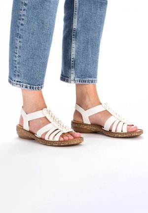 White strappy sandals with a textured brown sole, featuring a decorative beaded strap across the front and a cushioned footbed.