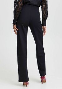 Schwarze maßgeschneiderte Hose mit geradem Bein aus glattem Stoff. Sie hat eine hohe Taille und wird mit roten High Heels kombiniert.