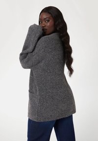 Cardigan gris, oversize, en tricot avec des manches longues et des poches avant. Texture douce, design mi-long et coupe décontractée.