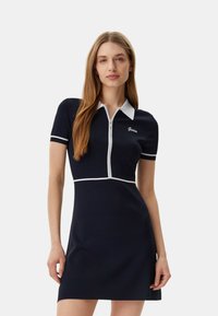 Laivaston lyhythihainen mekko, jossa on polo-kaulus, vetoketju edessä, valkoiset yksityiskohdat ja Guess-logo brodeerattuna rintaan. Mekko on muotoiltu tiiviisti.