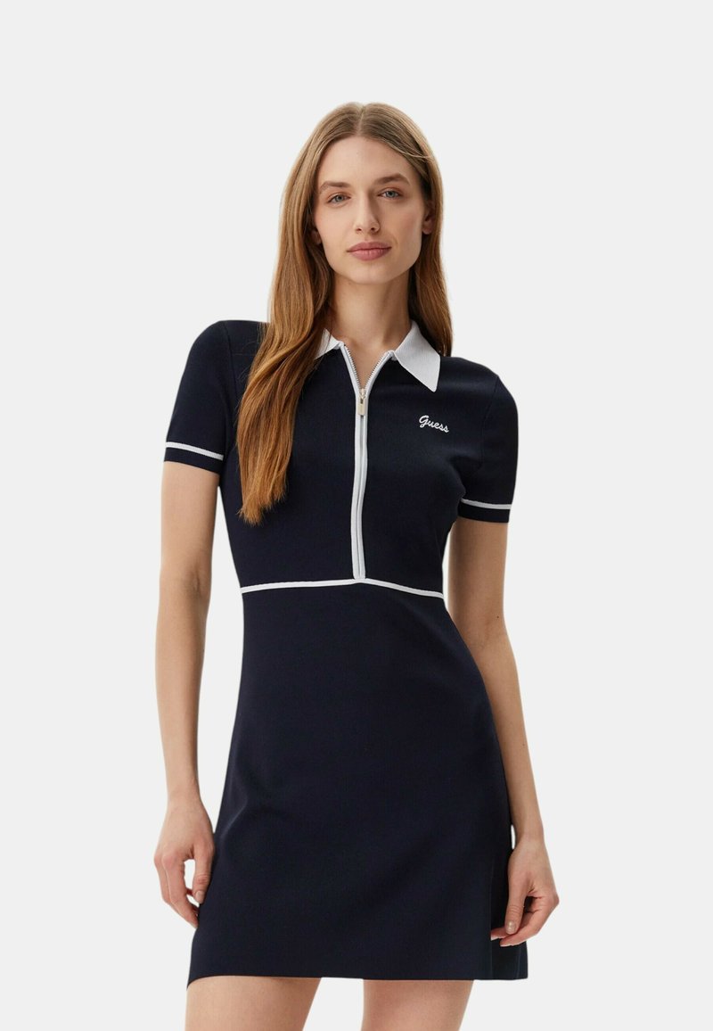 Laivaston lyhythihainen mekko, jossa on polo-kaulus, vetoketju edessä, valkoiset yksityiskohdat ja Guess-logo brodeerattuna rintaan. Mekko on muotoiltu tiiviisti.
