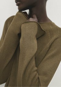 Pull en maille vert olive à coupe ample, avec des manches larges et repliées ainsi qu'un motif texturé, offrant une apparence douce et confortable.