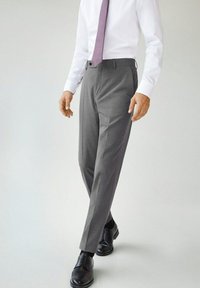 Grijze maatwerkbroeken met een gladde textuur, voorzien van een rechte pasvorm en riemlussen, gecombineerd met zwarte leren nette schoenen en een paarse stropdas.
