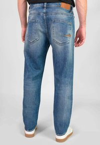 Blauwe denimjeans met een ontspannen pasvorm, voorzien van achterzakken, subtiele vervaging en een bruine leren patch op de tailleband.