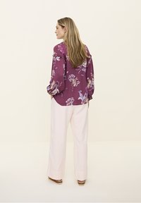 Blumenmuster, lila Bluse mit Rüschensäumen, kombiniert mit hellrosa weiten Hosen. Strukturierten Stoff, lockere Passform und entspannte Silhouette.