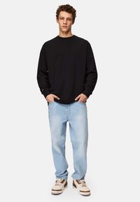Black long-sleeve shirt with a crew neckline, paired with light blue loose-fit jeans and white sneakers with brown accents.