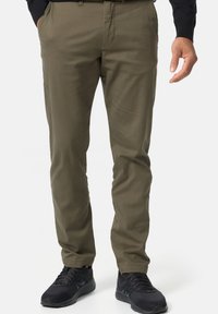 Pantalones caqui de corte recto, hechos de una tela suave. Presentan bolsillos frontales y un diseño de frente plano, combinados con zapatillas deportivas negras.