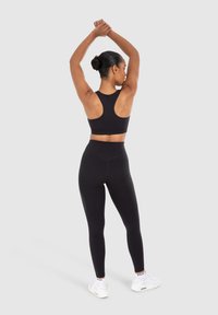 Zwarte sportbeha en hoge taille legging van rekbare stof. Beschikt over een racerback ontwerp en een gladde textuur, gecombineerd met witte sneakers.