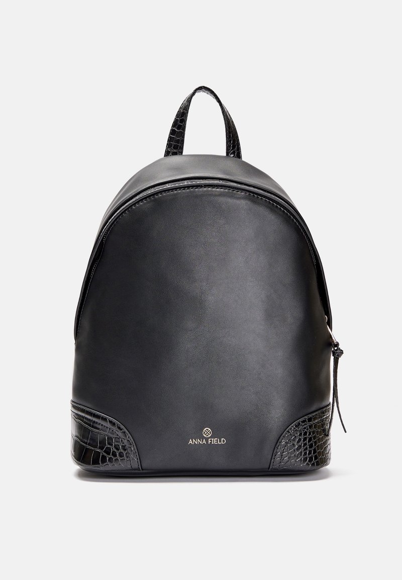 Sac à dos noir en simili cuir avec accents texturés aux coins, poignée supérieure, fermeture éclair et logo "Anna Field" au centre devant.
