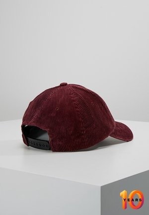 Ciemnoczerwona sztruksowa czapka bejsbolowa z regulowanym czarnym zapięciem typu snapback, umieszczona na białej powierzchni na szarym tle.
