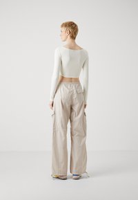 Top scurt dintr-un material crem deschis cu mâneci lungi, asociat cu pantaloni cargo bej deschis, cu buzunare laterale și talie elastică.