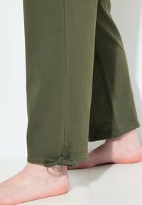 Zelené bavlněné kalhoty se střihem rovného nohavice, zdobené vázáním u kotníku. Hladká textura a jednoduchá konstrukce.