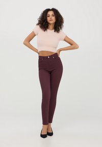 Maglione corto rosa chiaro con maniche corte, abbinato a jeans skinny a vita alta di un borgogna scuro. Tacchi a punta neri completano l'outfit.