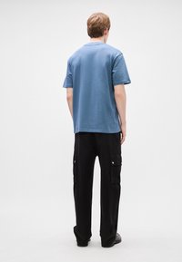 Μπλε βαμβακερό T-shirt με κοντά μανίκια, συνδυασμένο με μαύρα cargo παντελόνια που διαθέτουν δύο πλαϊνές τσέπες και κούμπωμα με κουμπί.