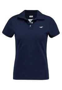 Mörkblå polo skjorta tillverkad av elastiskt tyg, med krage av klassisk stil, treknäppning och en liten vit logotyp på bröstet.