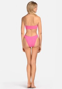 Różowy biustonosz w stylu bikini bez ramiączek z teksturowanej tkaniny, z wysokim stanem i minimalnym kryciem. Widok od tyłu.