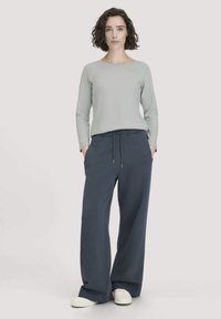 Hellgraues Langarmtop, kombiniert mit dunkelblauen weit geschnittenen Hosen. Das Outfit zeichnet sich durch eine lockere Passform und einen Zugbandbund aus weichem Stoff aus.