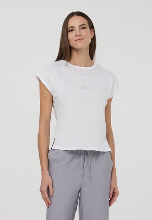T-shirt bianco a maniche corte con scollatura rotonda, caratterizzato da un motivo di strass sparsi nella parte superiore e fessure laterali. Testo decorativo sotto il design.