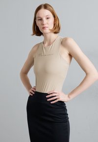 Beige sobiv T-särk kõrge kaelusega, millel on tagasihoidlik logo, koos musta kitsas seeliku siluetiga, millel on sile tekstuur.