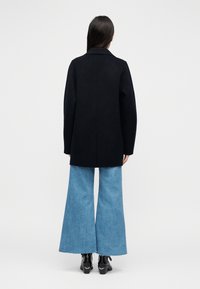 Mustast ülisuurest villast mantlist, millel on sälguga krae, villa ja teiste kiudude segu ning sirge lõige, koos helesiniste lõhestatud teksade ja mustade kingadega.