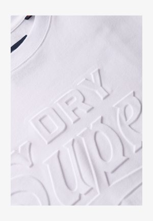 T-shirt en coton blanc avec des lettres en relief portant les mots "DRY" et "SUPER" dans une police moderne et audacieuse. Texture lisse, encolure ronde.